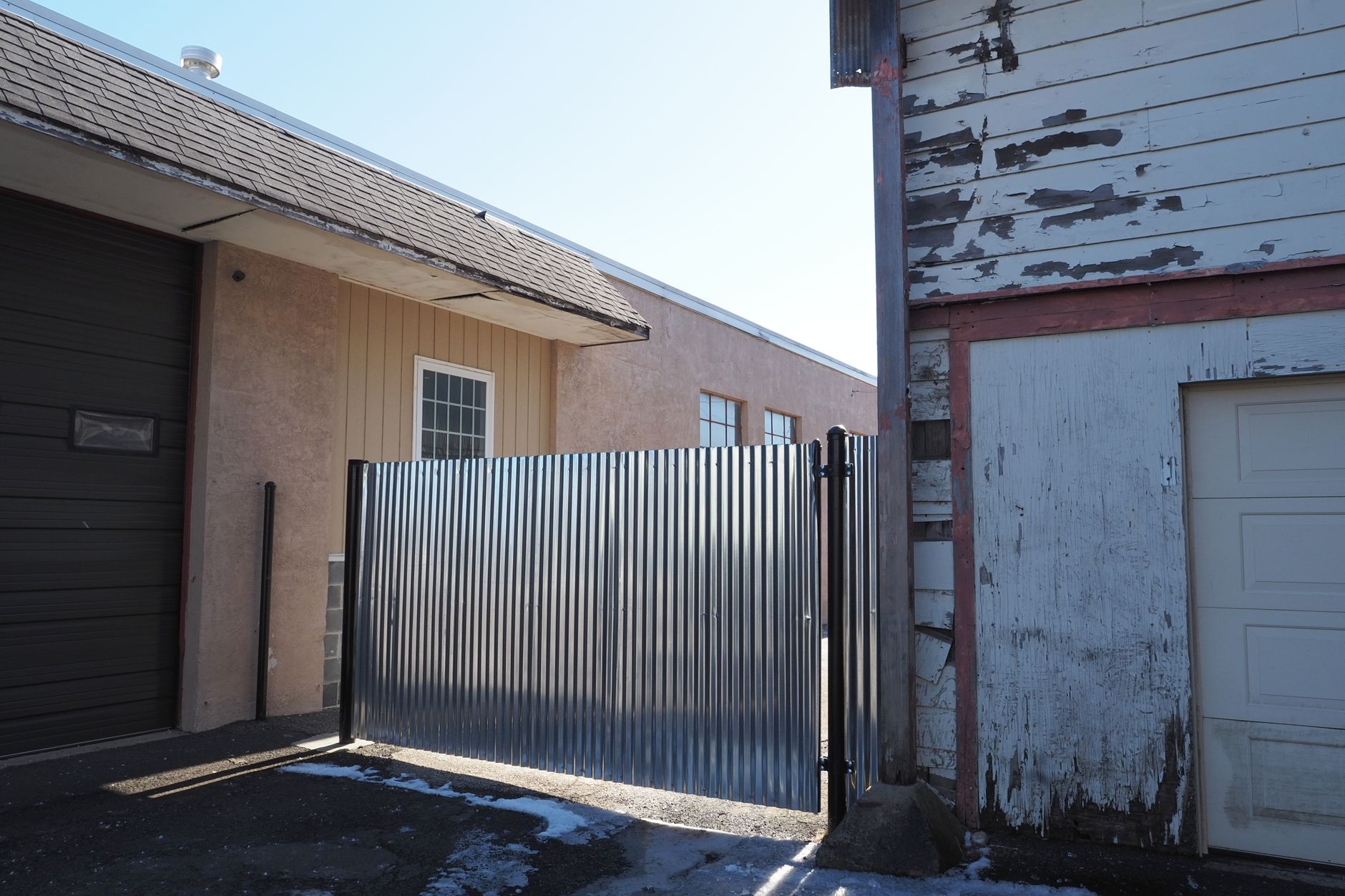 A black steel driveway gate standing open at the end of a residential driveway with a stone pillar and live in Austin, TX